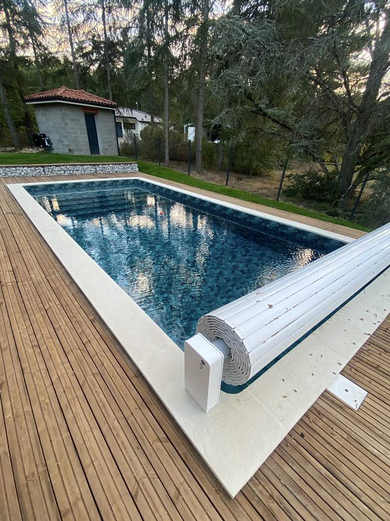 Piscine en membrane armée avec volet roulant, margelles claires et terrasse bois à Castelnau-d'Estrétefonds