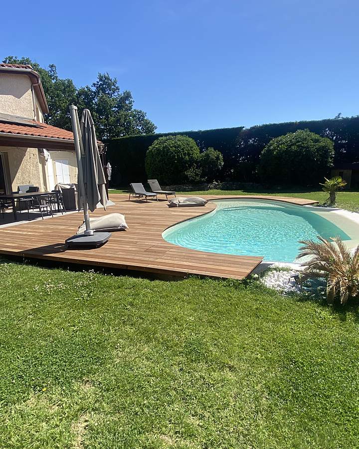 Piscine en forme de haricot bordée d'une terrasse en bois et d'une pelouse, chantier Seau Piscines de mai 2026