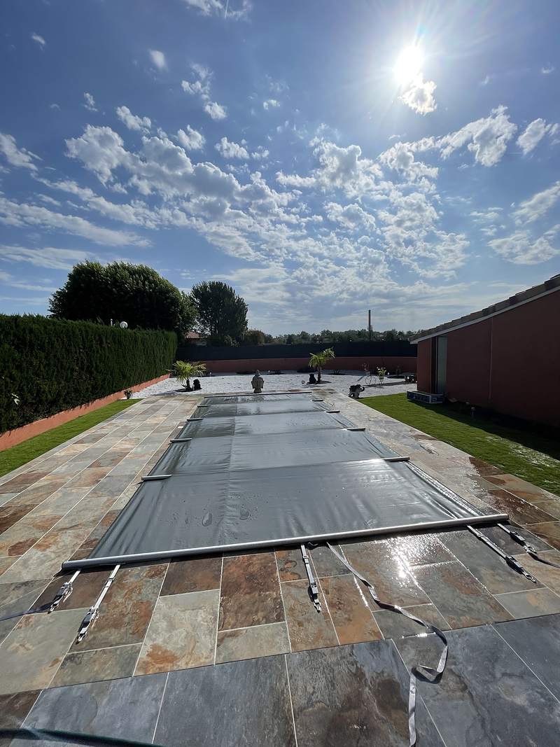 Bâche à barres de sécurité posée sur une piscine bordée de dallage en ardoise